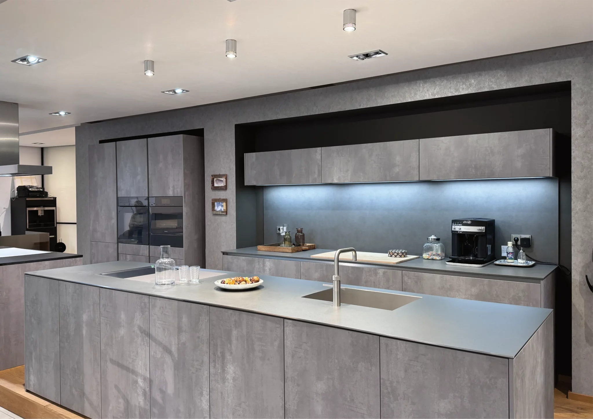 Moderne Ausstellungsküche in edler Betonoptik mit grifflosen Fronten, Kücheninsel, Einbaugeräten und stilvoll integrierter LED-Beleuchtung – exklusiv im Showroom von Kouker Küchen in Kempen.
