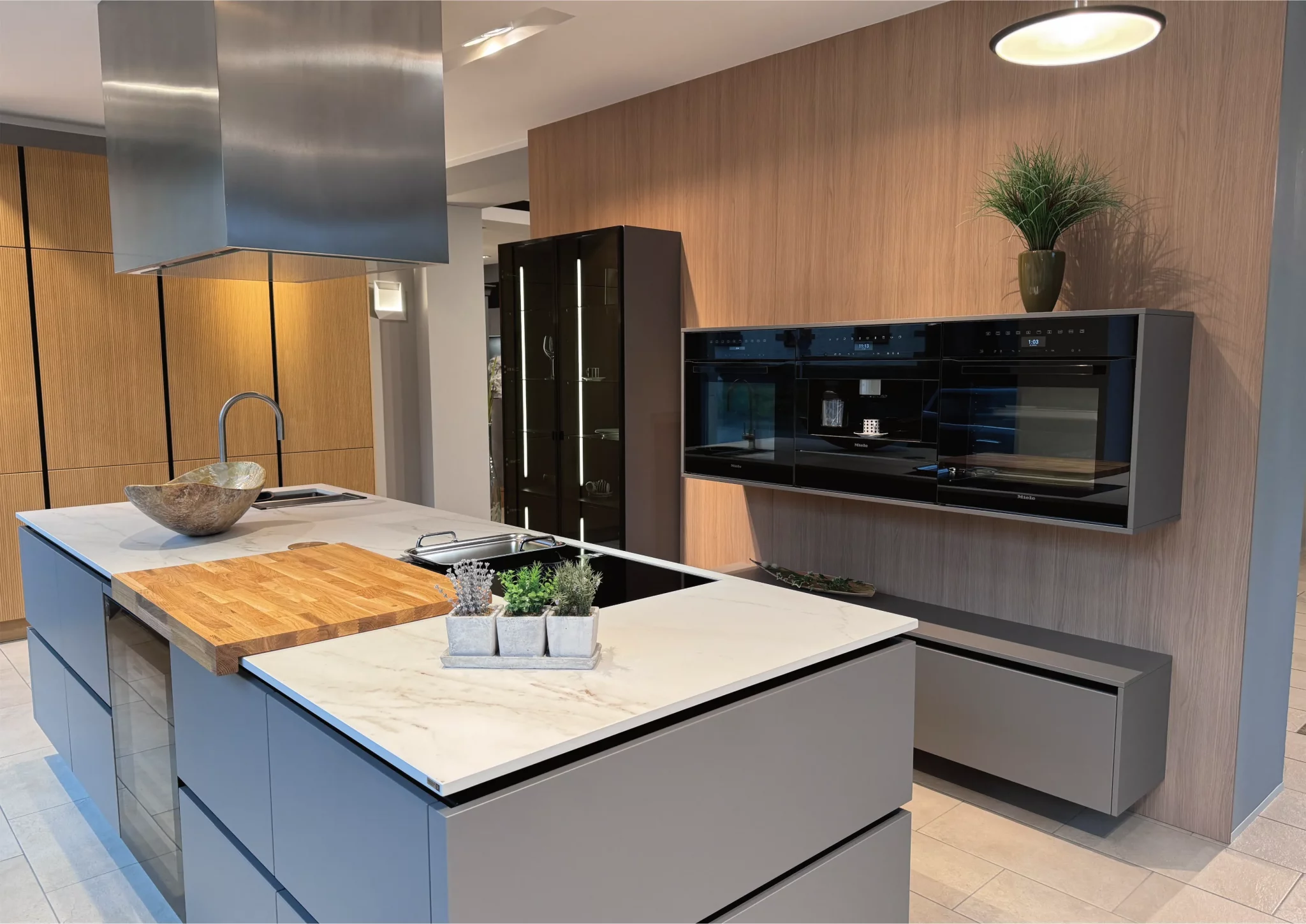 Moderne Einbauküche in hellem Grau mit Kücheninsel, integriertem Kochfeld, Marmor-Arbeitsplatte und deckenhohen Schränken, minimalistisch gestaltet.